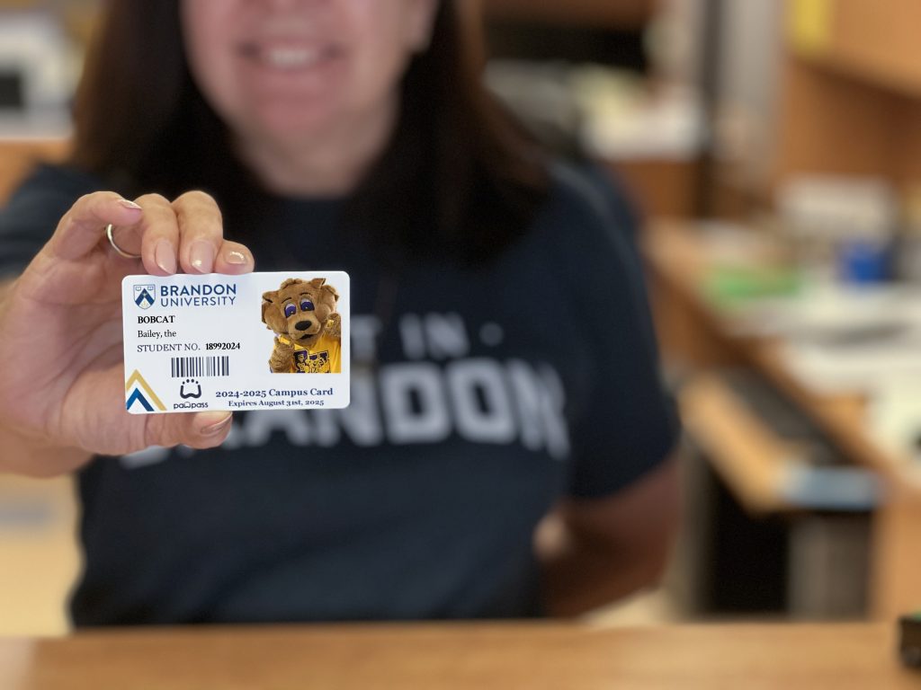 A woman holds a student ID card. The card features the university mascot, a cartoon bobcat named Bailey.